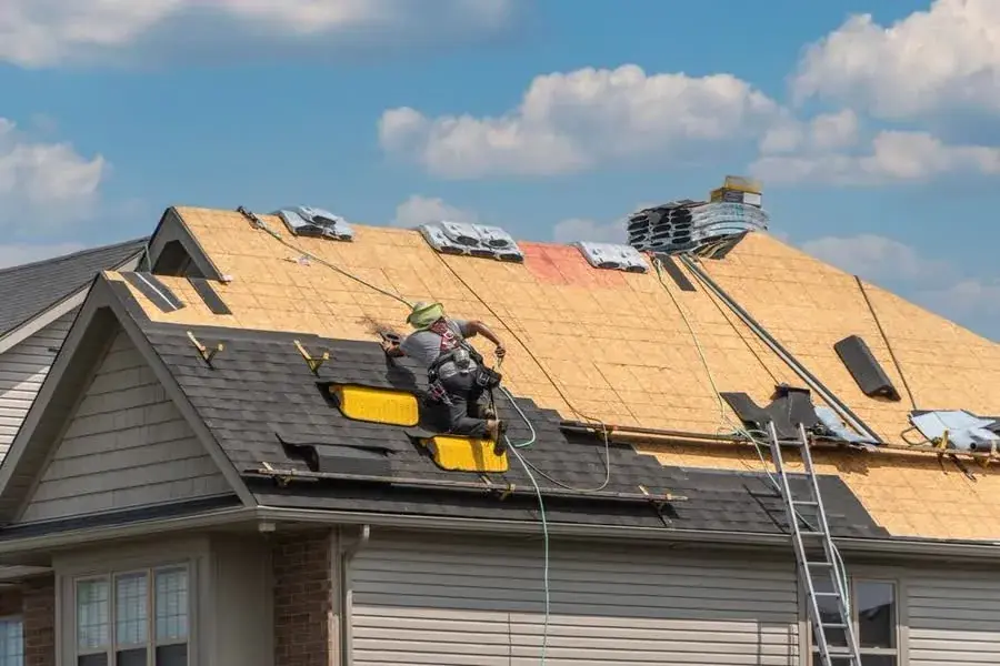 A roofer installing underlayment over new decking on a steep roof