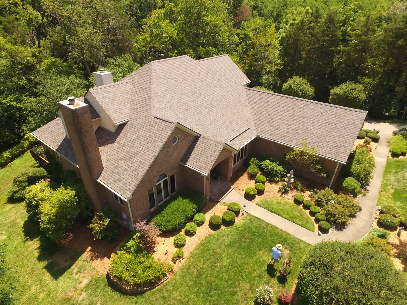 Drone photo of a brick home in the woods with a new brown shingle roof