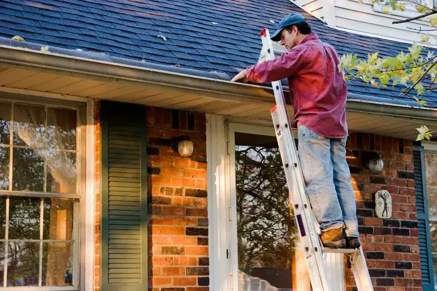 A man on a ladder cleaning the gutter of a brick home