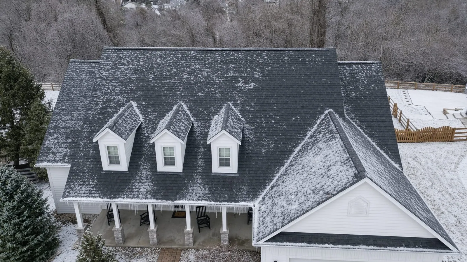 Illustration of a white home with three dormers in winter, with frost on the dark shingle roof and icicles along the porch gutter