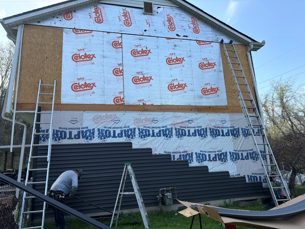 Installer fitting dark gray vinyl siding over house wrap on a gable wall