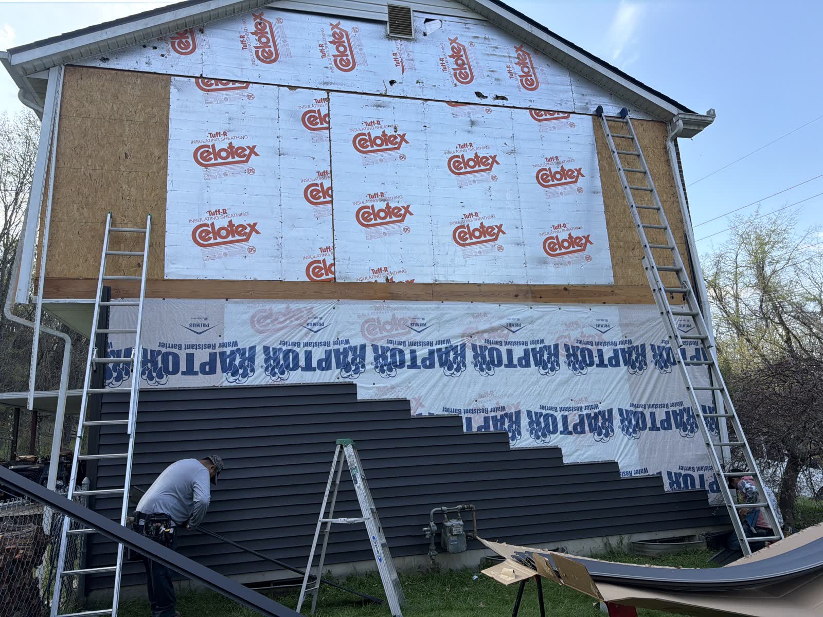 An installer fitting new gray vinyl siding over house wrap on the side of a home