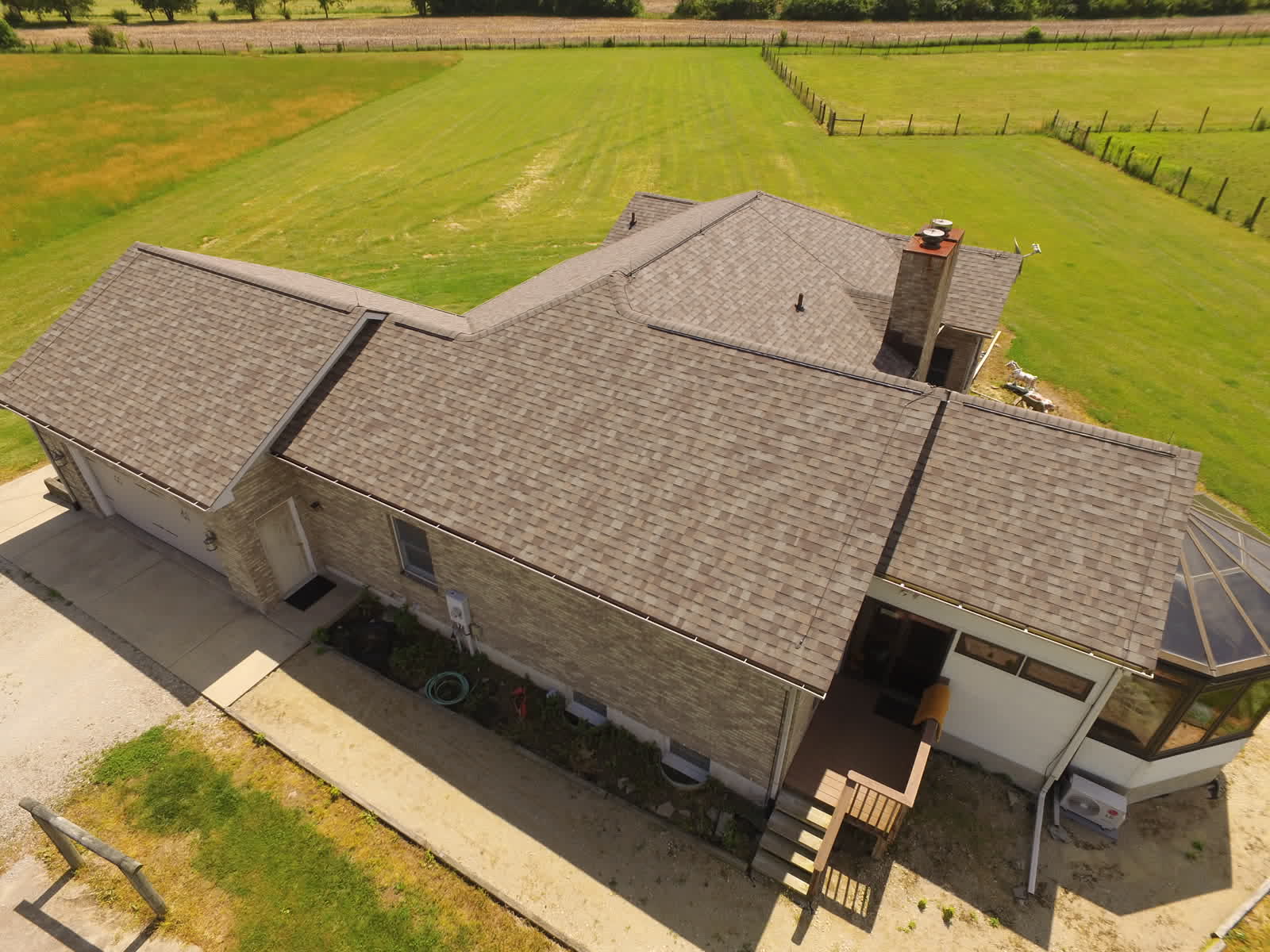Drone photo of a new brown shingle roof on a ranch home beside open fields
