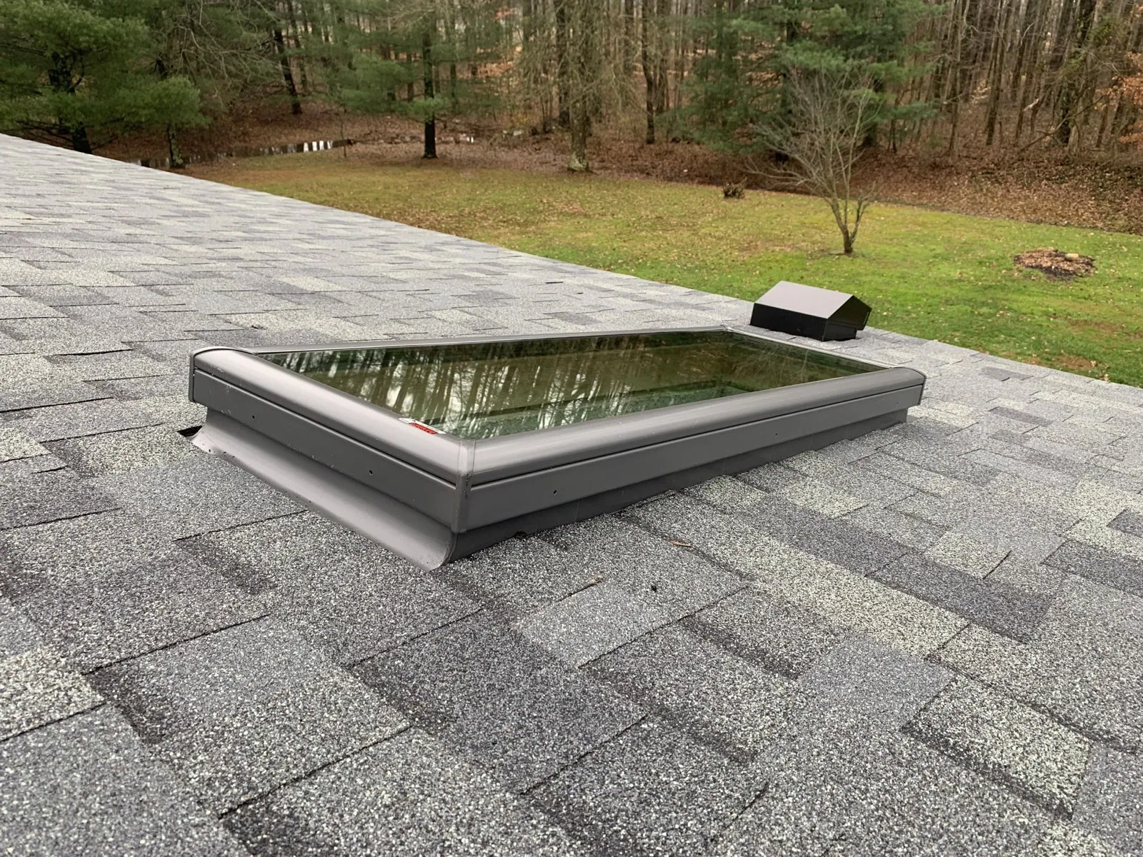 A newly installed skylight flashed into a gray shingle roof, with woods behind the home