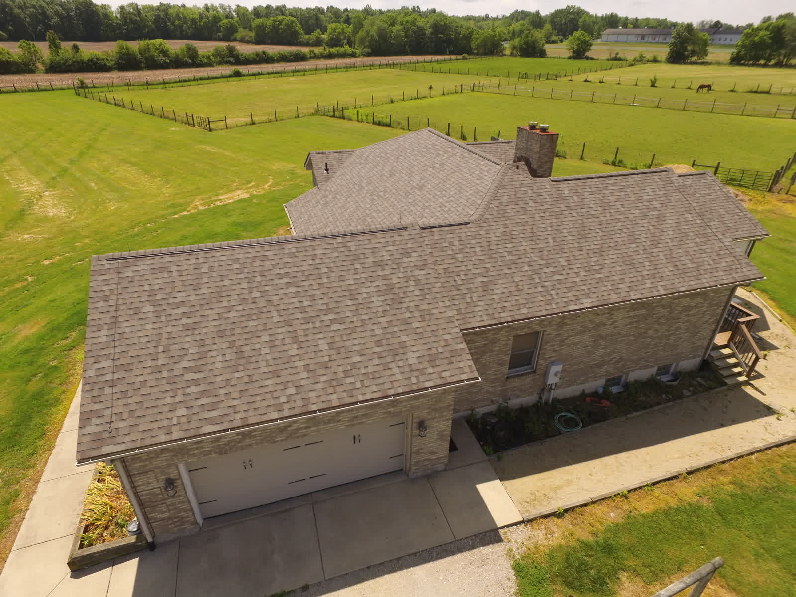 Drone photo of a ranch home with a new brown shingle roof beside open fields