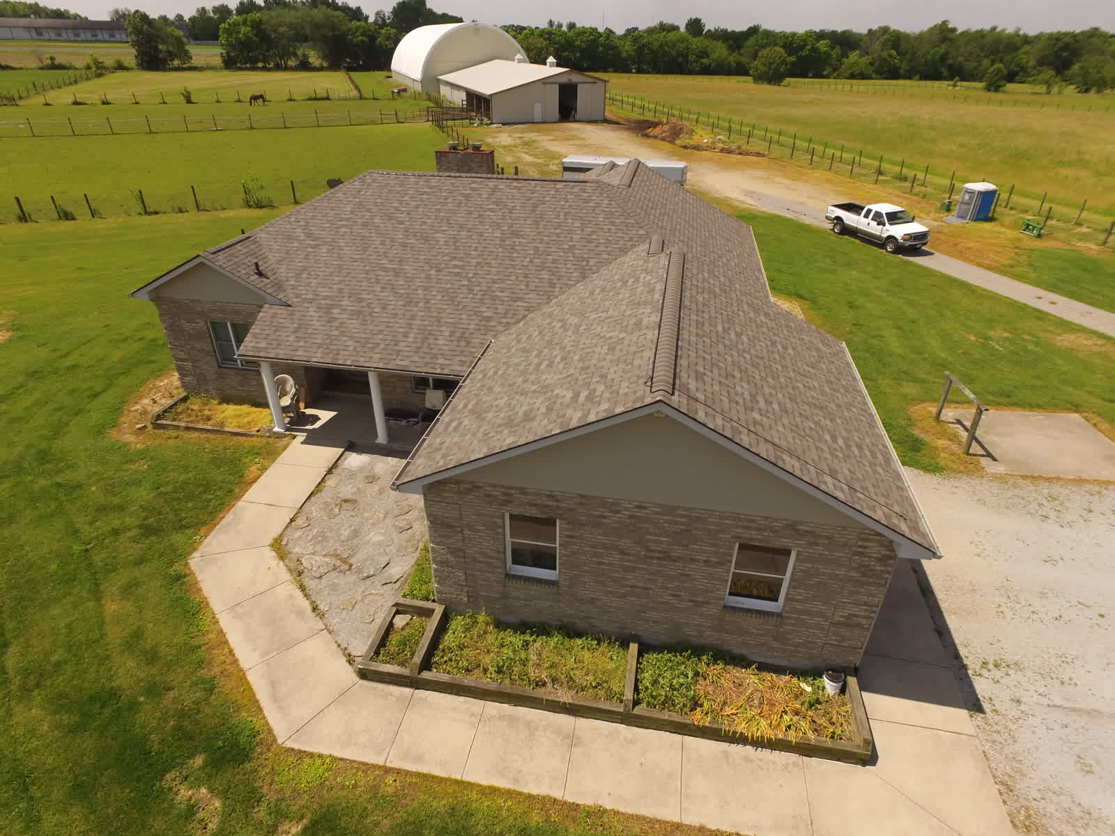 Drone photo of a ranch home with a new shingle roof and a long driveway