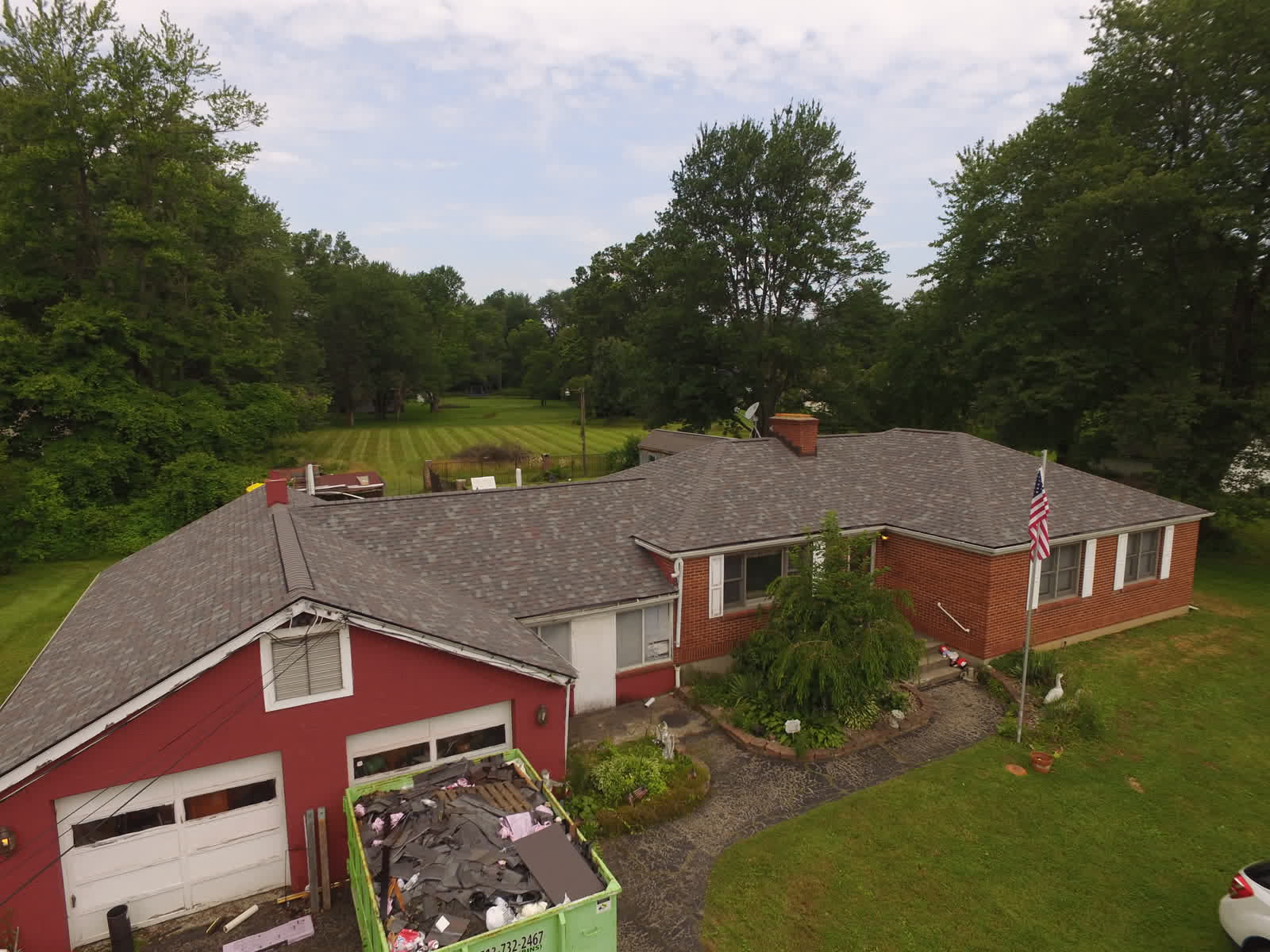Drone photo of a red brick ranch with a dumpster in the driveway during a roof replacement