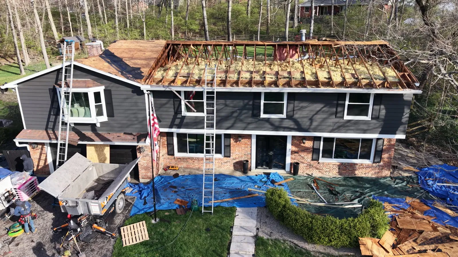 Drone photo of a roof tear-off with tarps protecting the yard and a debris trailer at the house