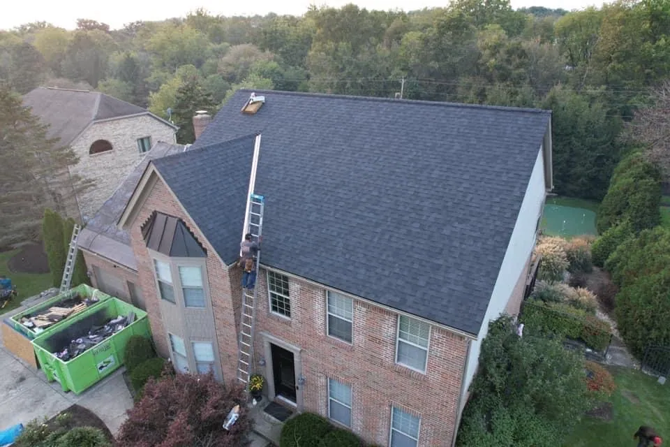 Roofer on a ladder at a two-story brick home with a new shingle roof