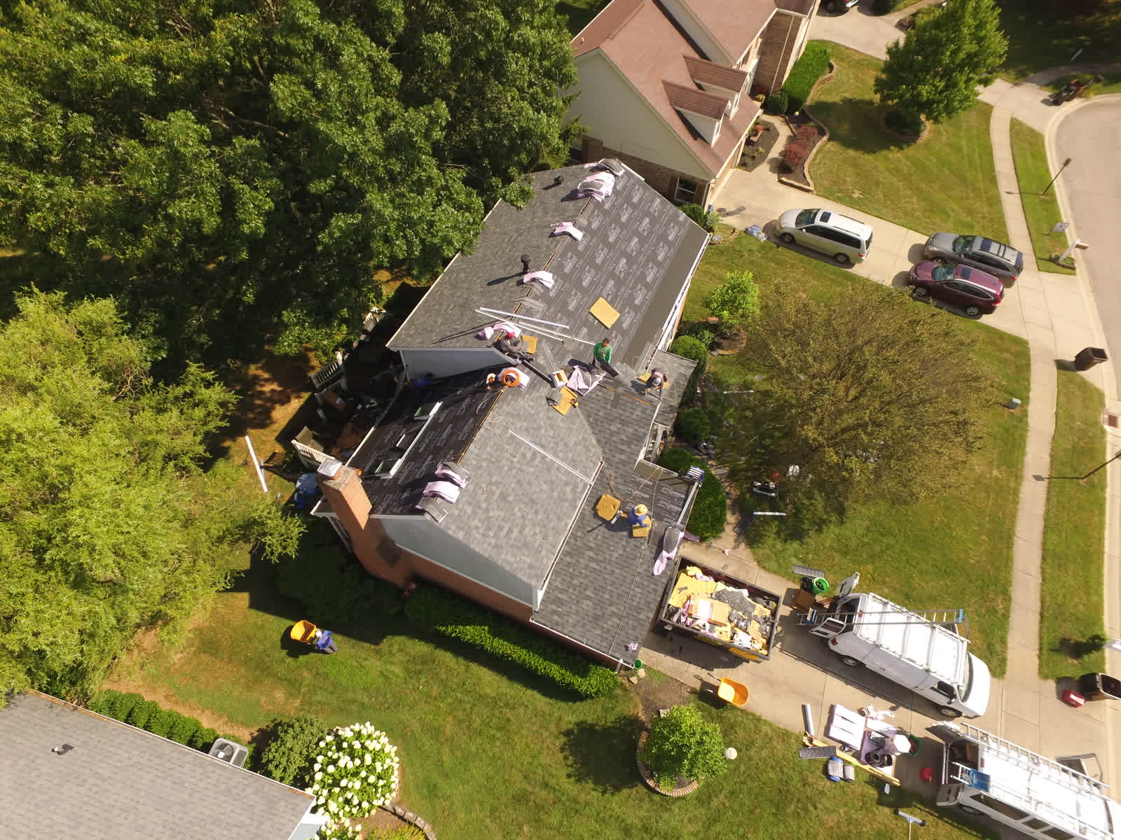 Roofers finishing a gray shingle roof on a two-story home