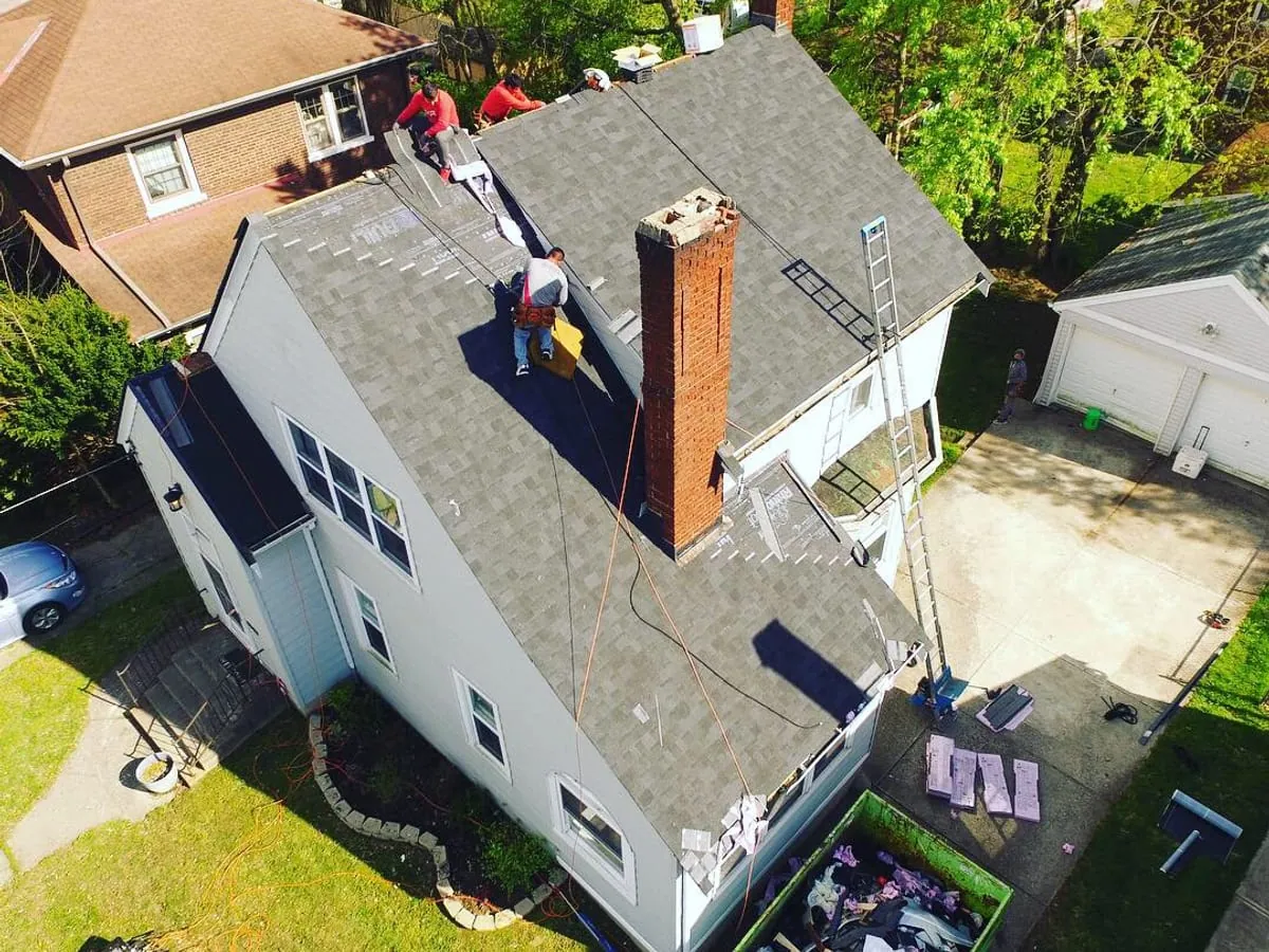 Drone photo of roofers repairing a shingle roof beside a brick chimney