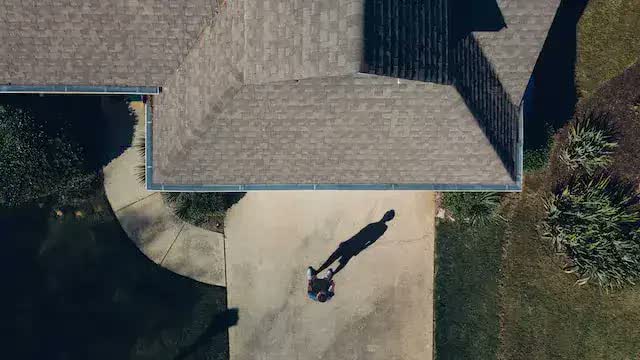 Overhead drone photo of a shingle roof with the drone pilot's shadow on the driveway