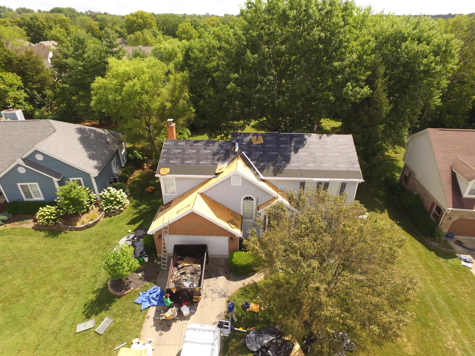 Two-story home with roof decking exposed and a dumpster in the driveway