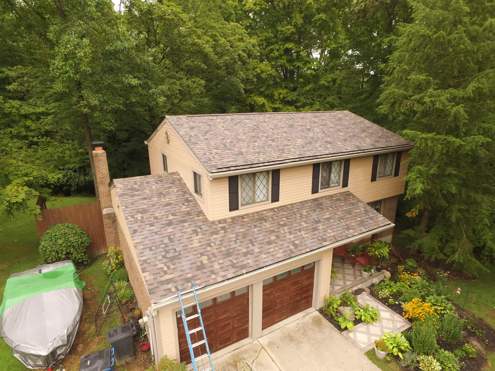 Drone photo of a two-story home with a tan shingle roof and a ladder at the eave