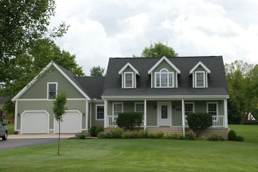 A green two-story home with dormers and a dark shingle roof