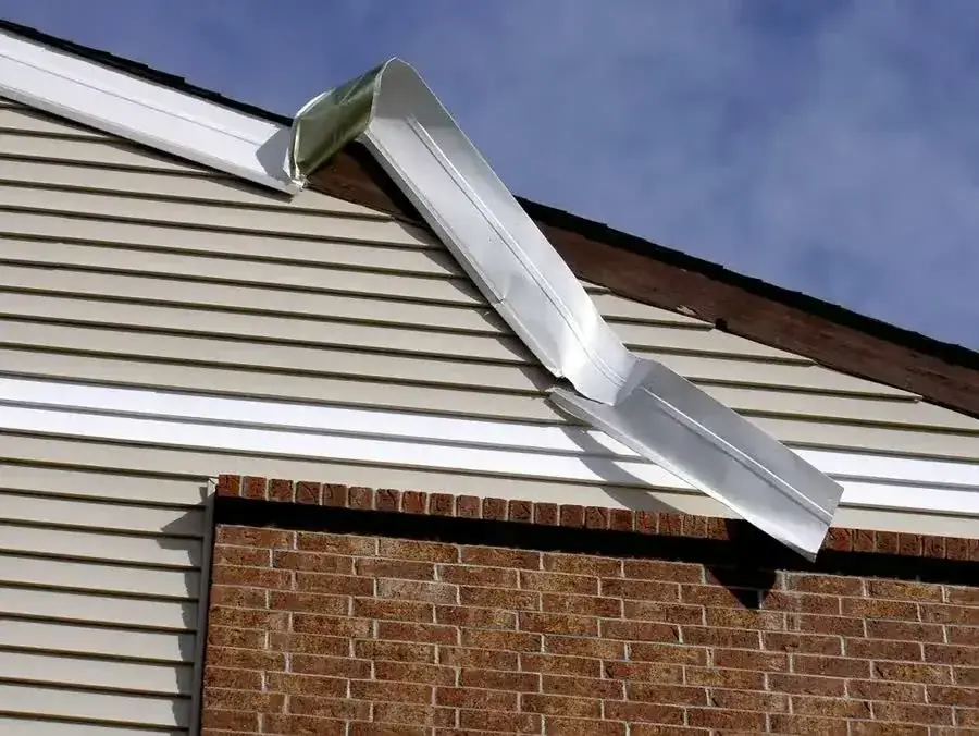 A strip of trim hanging loose from vinyl siding above a brick wall